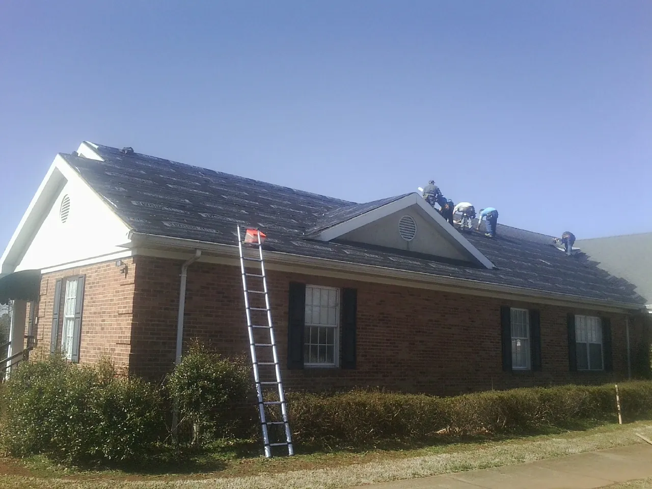 Crew tearing shingles off a brick ranch roof with a ladder set — Emergency Roof Repair work by our crew in Boxford