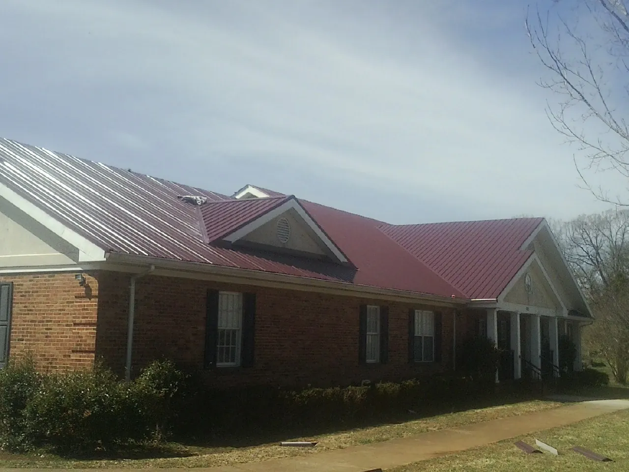 Red metal roof with gabled entries on a long brick building, from a Hail Damage Roof Repair job in Boxford