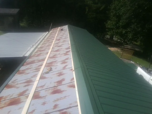 Old rusted panels beside newly installed green metal roofing — Wind Damage Roof Repair by Roofing Brothers in Boxford