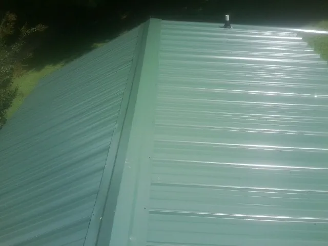 New green metal panels meeting at the ridge of a roof — Flat Roof Repair work by our crew in Boxford