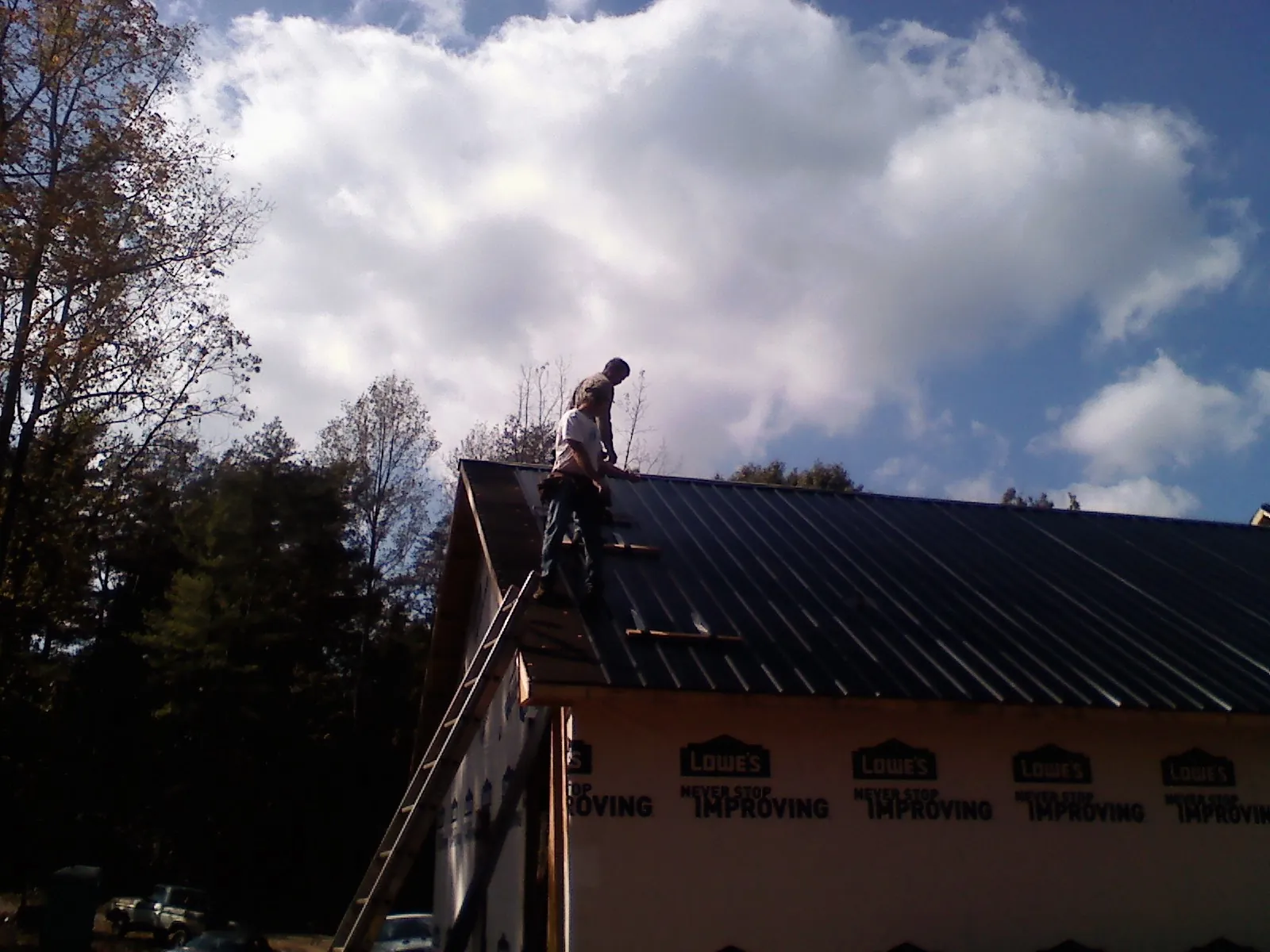 Roofer fastening dark metal panels high against a cloudy sky, from a Roof Inspection job in Boxford