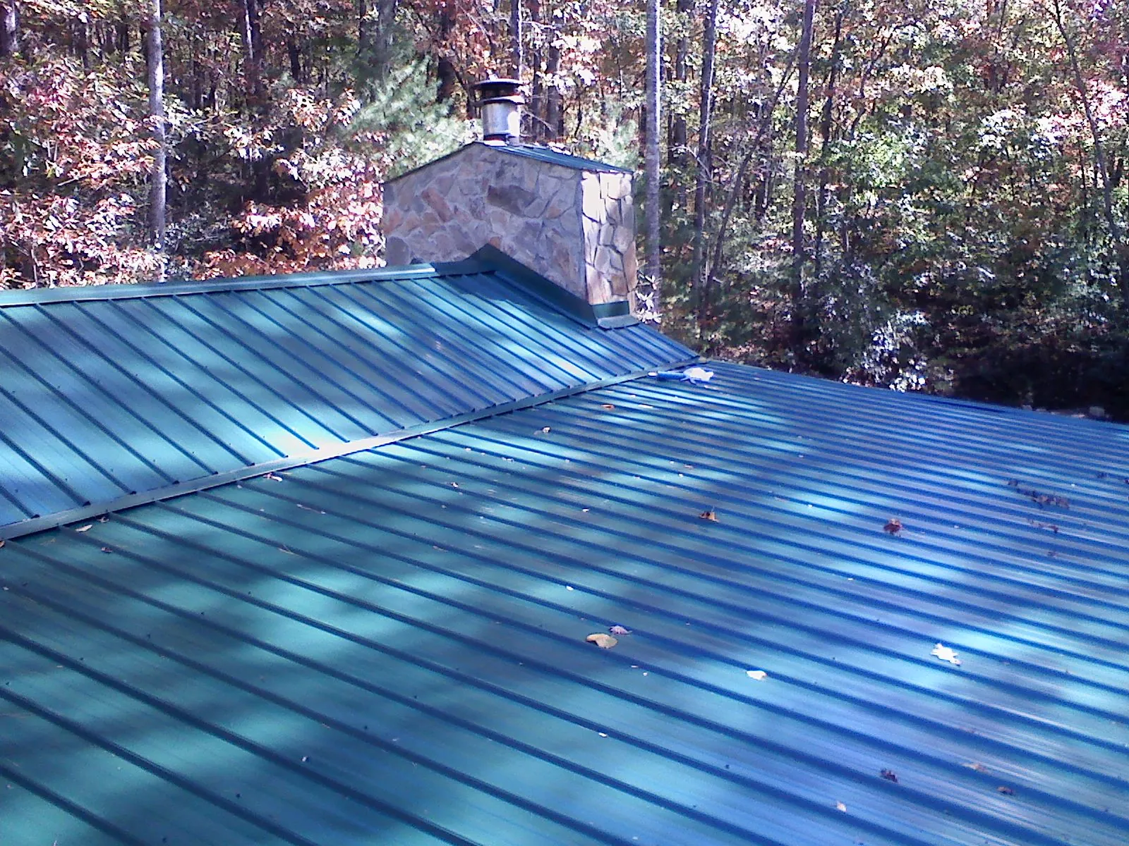 New green metal roof and stone chimney surrounded by autumn woods in Boxford
