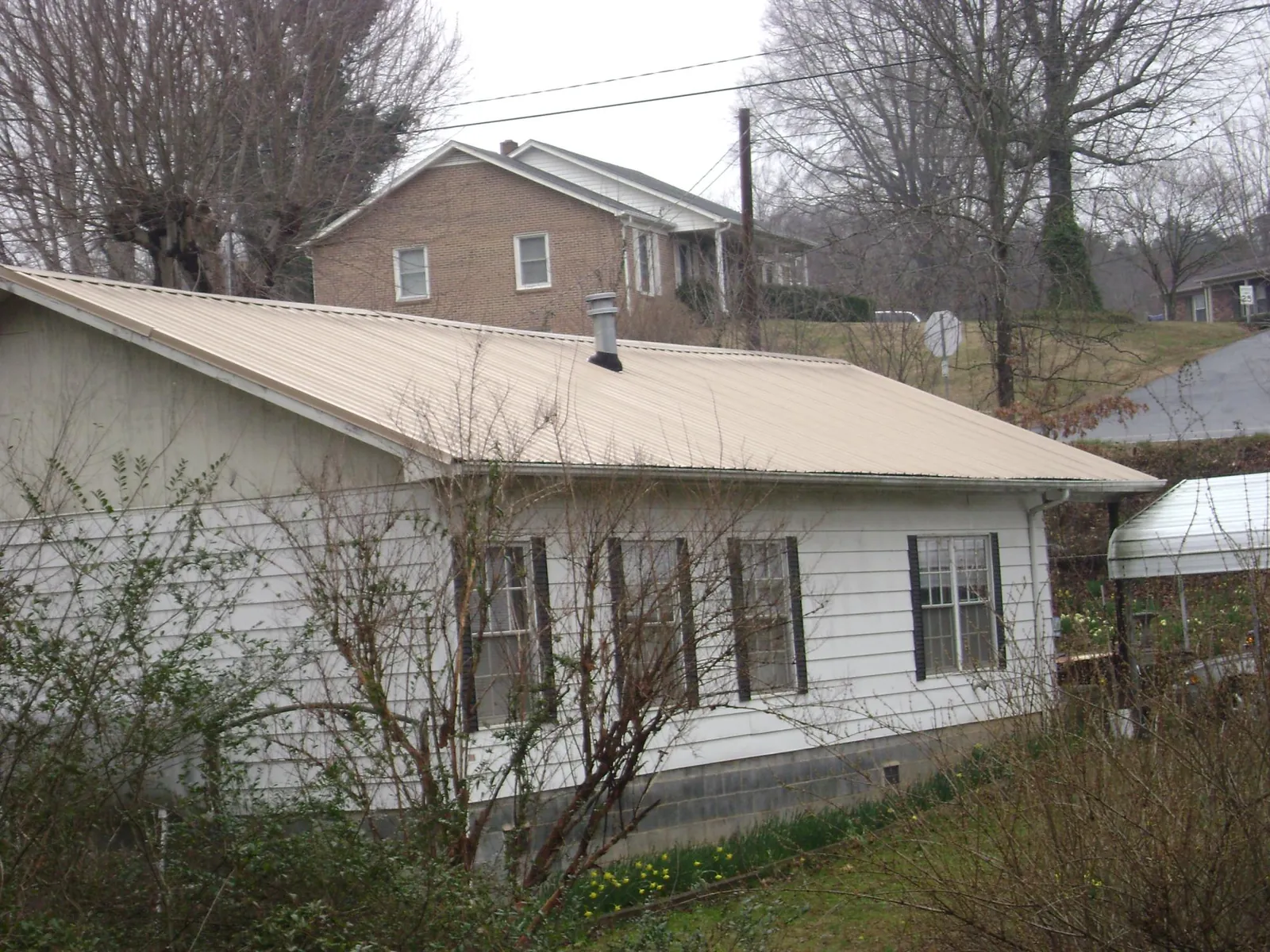 Tan metal roof on a white sided house set into a hillside — Commercial Roofing by Roofing Brothers in Boxford